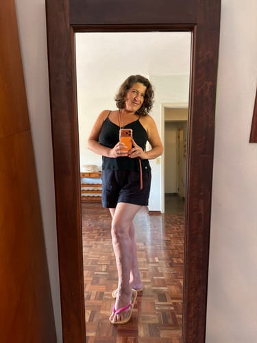 Avaliadora tirando uma selfie no espelho usando a Cordinha Odara cor de pêssego em volta do pescoço.