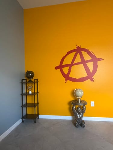 Customer's red Anarchy A Symbol Vinyl Decal Sticker on a bright yellow wall in a room corner.