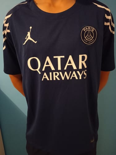 Client montrant la face avant d'un maillot de football bleu marine avec des logos blancs.