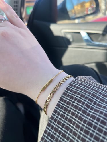 Reviewer's wrist showing the dainty, gold This World and the Next v2 Bracelet stacked with another chain.