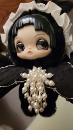 Close-up of a customer's black Viora Floraison Libre 'Iris' plush, showing its movable eyelids and pearl embellishment.