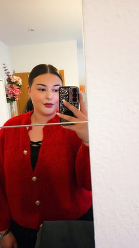Eine Kundin macht ein Spiegel-Selfie und trägt den roten Oversized Cardigan 'CozyGlam'.