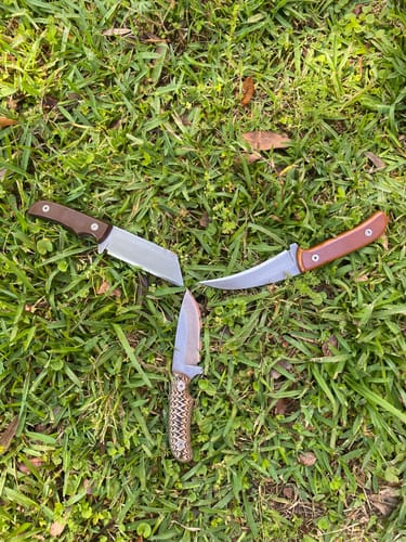 Reviewer's photo of three custom knives with polished blades arranged in a triangle on grass.