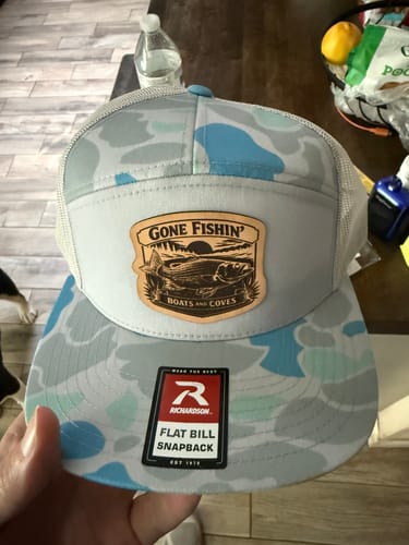 Customer holding a new Richardson 168P trucker hat with a blue camouflage bill and a custom 'Gone Fishin'' leather patch.