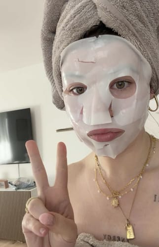 Kundin trägt die Kollagen Glow Maske und macht mit der Hand ein Peace-Zeichen.