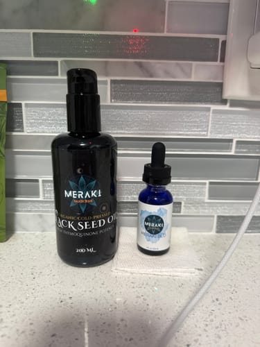 Customer's bottle of Black Seed Oil on a counter next to a smaller, blue dropper bottle.