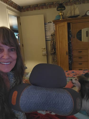 A smiling customer holds up the gray Callixe Thera Pillow in their bedroom.