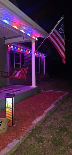 Customer's Betsy Ross Flag flown from a home's porch at night, illuminated by patriotic red and blue lights.