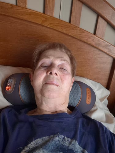 Customer relaxing in bed with eyes closed while using the Original Callixe Thera Pillow around their neck.