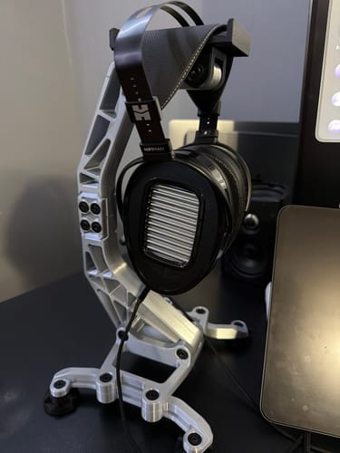 Customer's Hifiman Arya Unveiled Headphones resting on a modern silver stand on a desk.