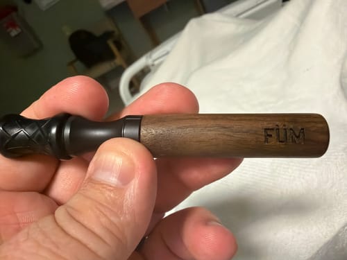 Close-up of a customer holding the FÜM Solano device, showing the walnut barrel and black mouthpiece.