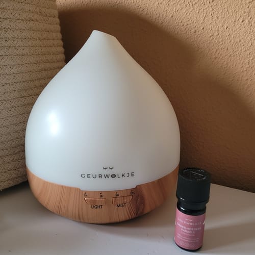 Recensent toont de 'Onder moeders paraplu' olie naast een verlichte Geurwolkje aroma diffuser.
