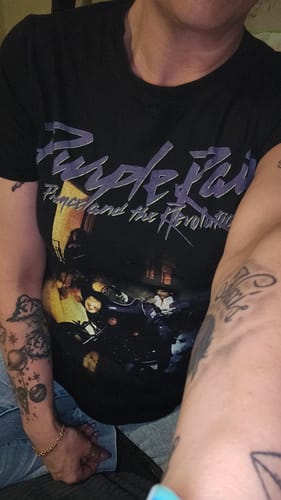 Customer wearing a black graphic Prince 'Purple Rain' t-shirt from the wholesale pack.