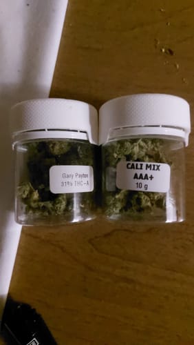 Customer's clear jar of CALI MIX AAA+ buds, with a visible label, on a wooden table.