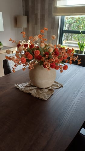 Recensent toont het volumineuze Wax Arrangement - Mix in een lichte vaas op een donkere eettafel.