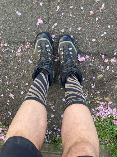 A reviewer's first-person view of their legs, wearing zebra-print Lucky Dip Compression Socks with dark hiking boots.