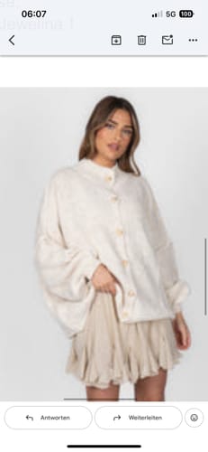 Eine Kundin trägt den cremefarbenen Oversized Cardigan "CozyGlam" über einem Rock.