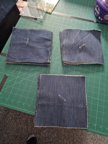 Customer's cotton denim fabric cut into square blocks and stacked on a green cutting mat for a quilting project.