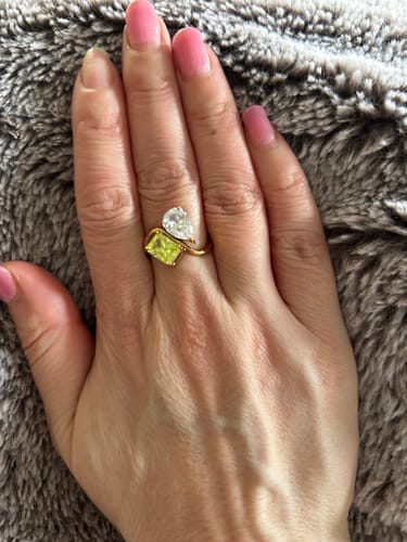 Customer's hand wearing the gold Navae Birthstone Ring with a clear pear-cut and a yellow radiant-cut stone.