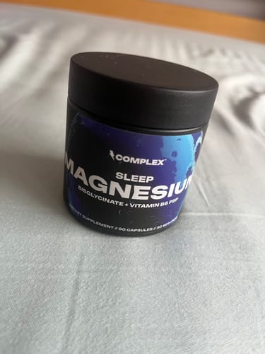Reviewer's black jar of Complex Sleep Magnesium resting on a light-colored bedsheet.