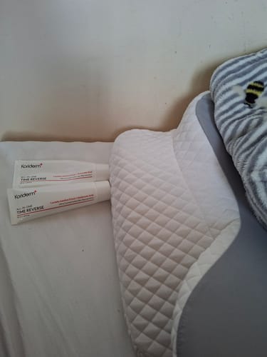 Customer's two tubes of Koriderm™ Time Reverse Cream lying on a white sheet next to a pillow.