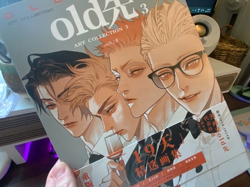 A reviewer holds the Old Xian 19 Days Art Collection 3, showing the illustrated cover featuring four characters.