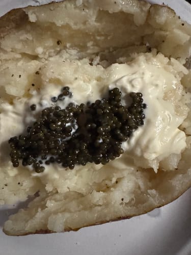 Customer's close-up of black caviar served on a baked potato with a creamy topping.