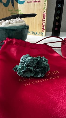 Reviewer's mesmerizing dark green crystal from the VIP Crystal Club, resting on a red pouch.