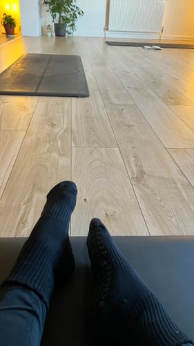 Customer's close-up view of their feet wearing black Dual-Direction Grip Basics socks in a yoga studio.