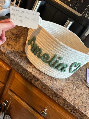 Customer holding a note next to a beautiful white rope basket personalized with the name 'Amelia' in green.