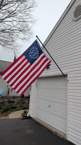Reviewer's 1776 to 2026 Betsy Ross Flag mounted on a flagpole on the side of a house.