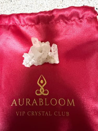 Customer's raw crystal cluster from the VIP Crystal Club resting on its red satin logo pouch.