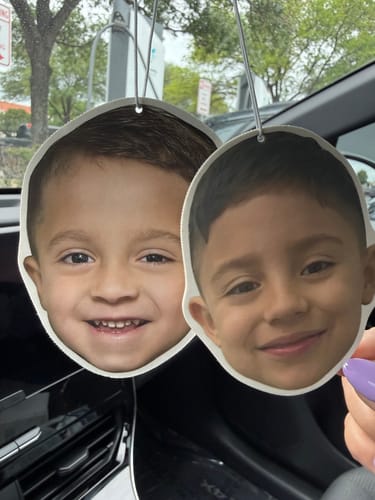 Customer holding two Custom Air Fresheners designed as cutouts of two children's faces, hanging inside a car.