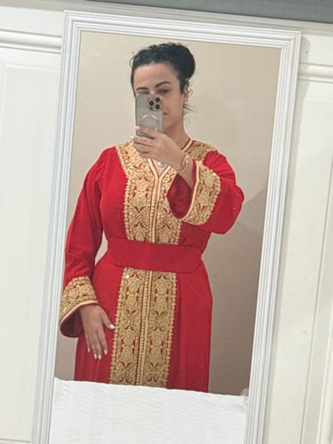 Reviewer in a mirror selfie wearing the red Caftan Sara, showing the fit with its matching belt and gold embroidery.