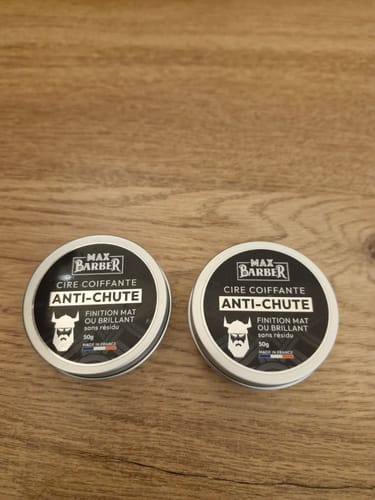 Photo d'un client montrant deux pots de Cire Coiffante Anti-Chute sur une surface en bois.