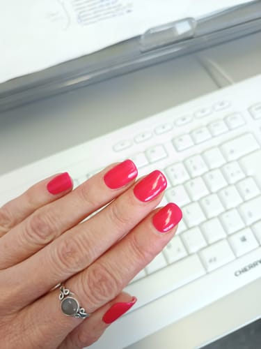 Hand einer Kundin mit manikürten Nägeln, die die glänzenden, pinken „Flamingo Frill“ UV-Gel-Folien trägt.