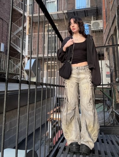Customer wearing the deconstructed flared patchwork jeans outdoors, styled with a black top, hoodie, and chunky platform shoes.