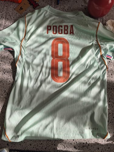 Photo d'un client montrant le dos d'un maillot de football vert clair avec le flocage orange 'POGBA 8'.
