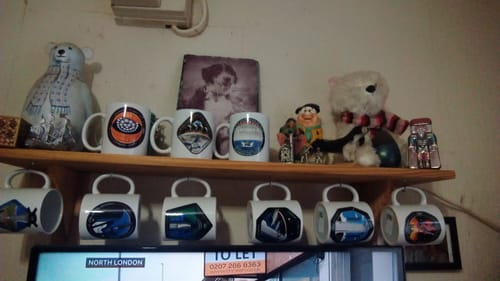Customer's Apollo To Artemis mug displayed on a full shelf as part of a large mug collection.