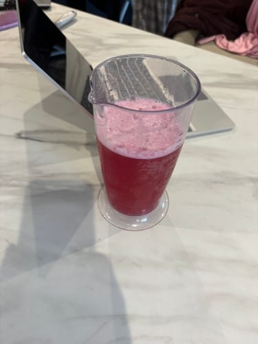 Customer's pink, frothy drink, part of the day + night combo, in a clear cup on a marble table.