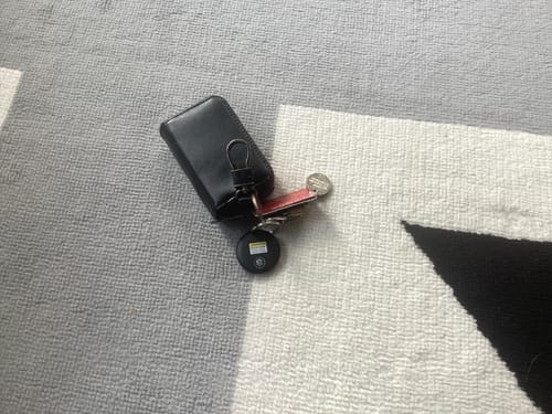 Customer's black SmartTag attached to a set of keys with a leather key fob, resting on a patterned rug.