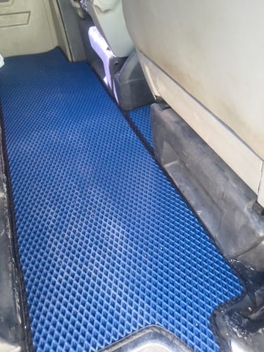 Recenzent pokazuje niebieskie, teksturowane dywaniki samochodowe idealnie dopasowane do podłogi vana.