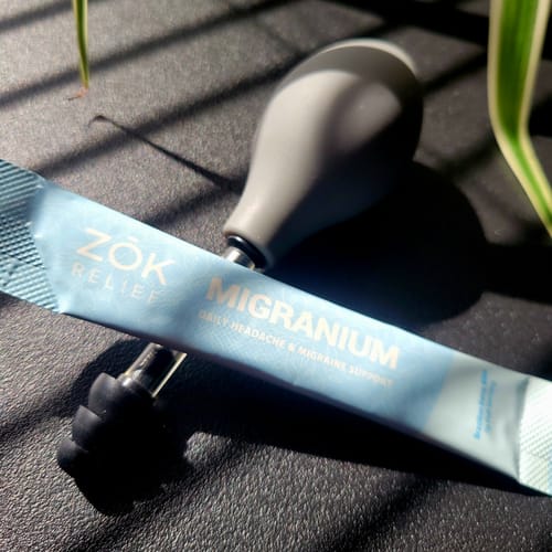 A reviewer's blue Migranium supplement sachet lying next to a ZOK pressure relief device.