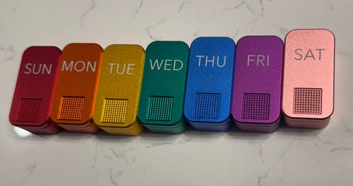 Customer's seven colorful metal pill cases arranged in a rainbow, labeled with the days of the week.