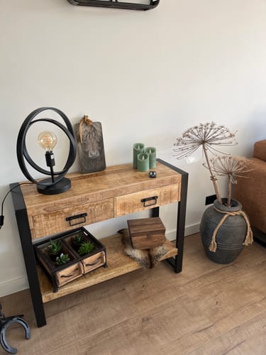 Klant toont de industriële sidetable van mangohout, ingericht met een lamp en decoratie in de woonkamer.