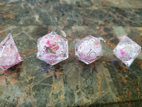 Reviewer's four clear resin Sakura dice lined up, showing the pink floral design inside their liquid cores.