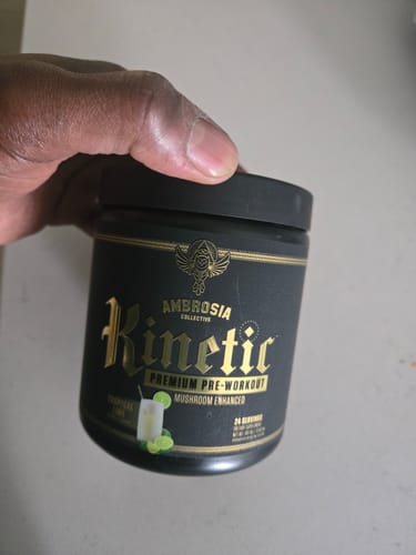 Reviewer holding the black tub of Kinetic Premium Pre-Workout in the Tropical Lime flavor.