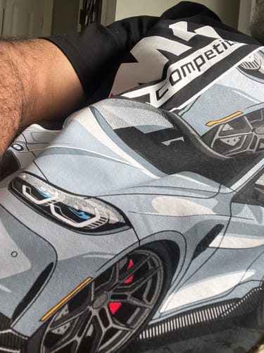 Close-up of a customer wearing a black t-shirt from the TCG93 MYSTERY CASH BOX, featuring a large graphic of a silver car.