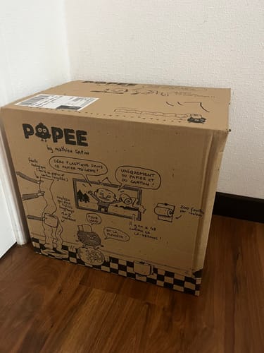Avis du client : la boîte en carton du papier toilette Zéro plastique, illustrée par Mathieu Sapin et posée au sol.