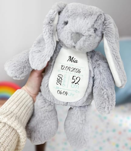 Ein Kunde hält einen flauschigen, grauen Plüschhasen, der personalisierte Geburtsdaten auf den Bauch gedruckt hat.